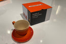Orange ceramic cup and saucer set with a matching box on a white surface